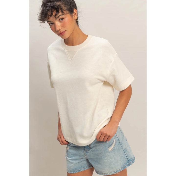 Woman wearing a white oversized sweater and denim shorts on a plain background