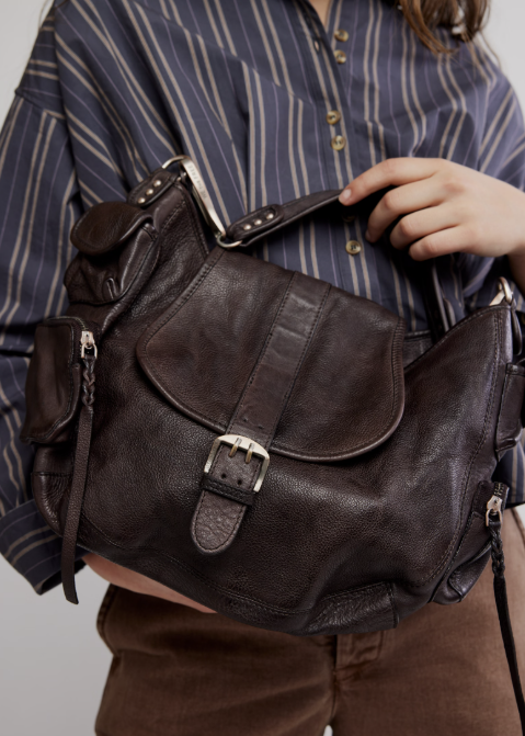 Woman holding large dark brown espresso color purse with stripe shirt and brown pants on
