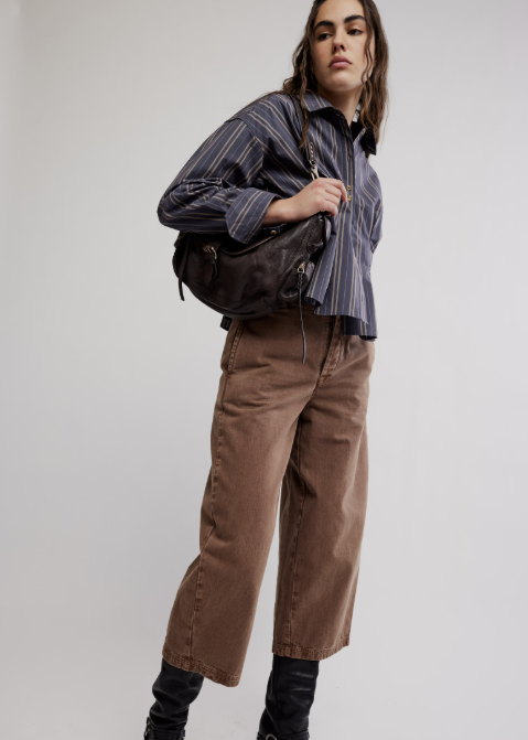 Woman wearing stripe shirt and brown pants modeling a large espresso brown purse on white background