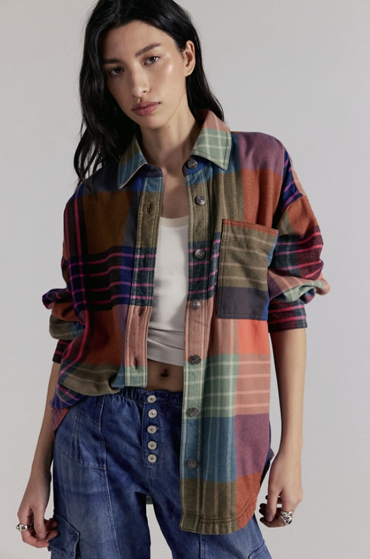 Person wearing a colorful plaid shirt over a white top and blue jeans on a plain background