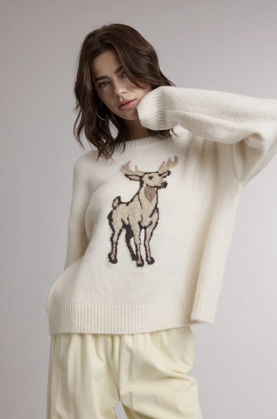 Woman wearing cream sweater with deer embroidery with yellow pants on plain background