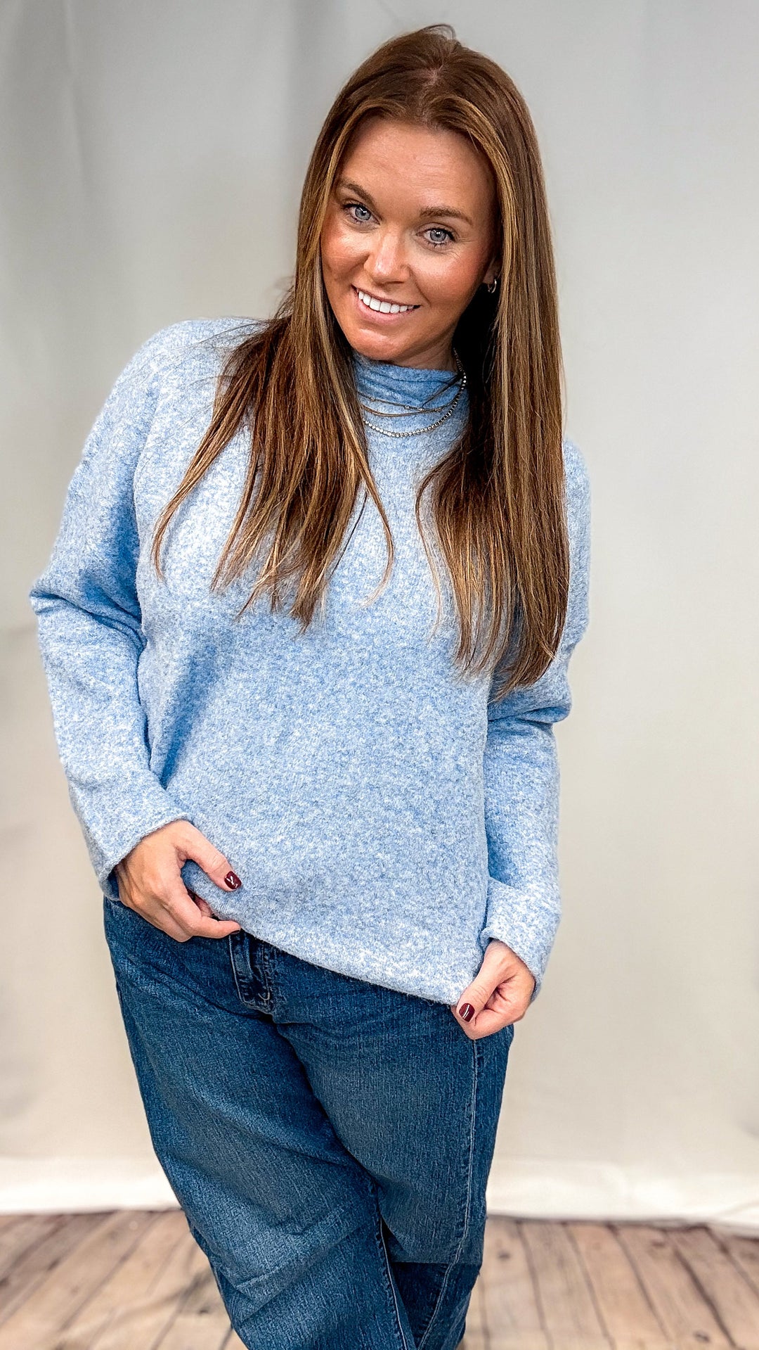Woman wearing blue mock neck pullover and jeans on plain background