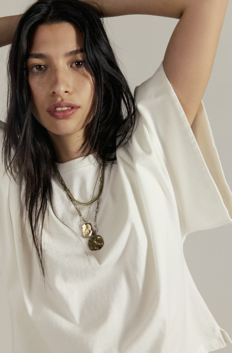 Woman wearing a white top and gold necklace with a neutral background