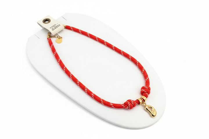 Cord necklace with gold bubble D on plain background
