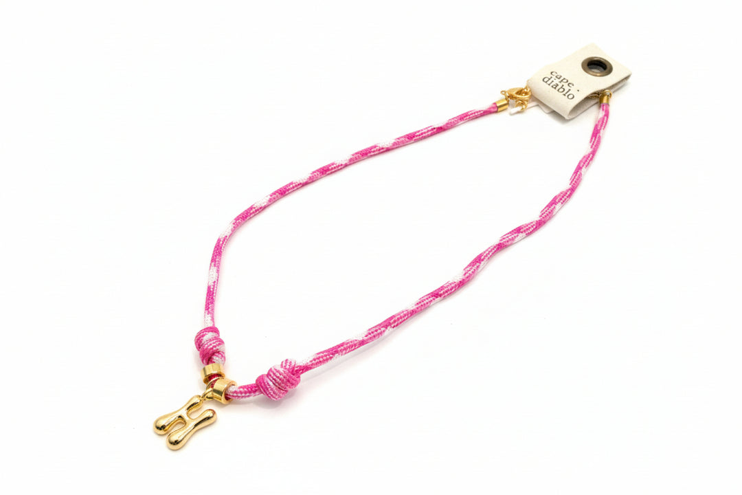 Cord necklace with gold bubble H on plain background
