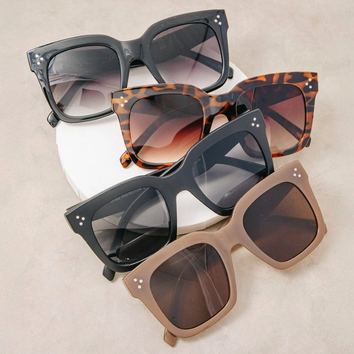 Four pairs of sunglasses in different styles and colors on a beige background