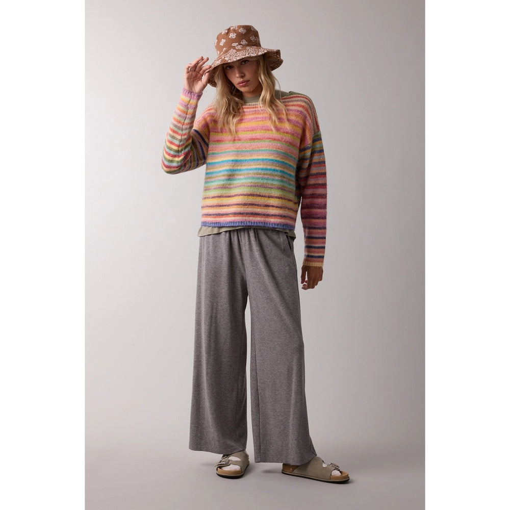 woman wearing rainbow sweater with grey pants and bucket hat on plain background