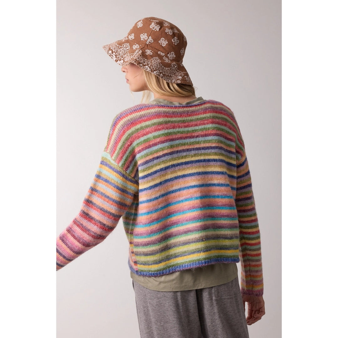 Person wearing a colorful striped sweater and patterned hat on a plain background
