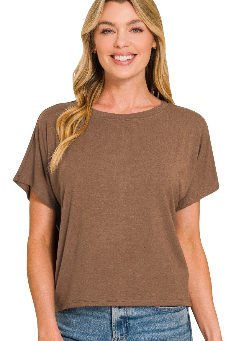 A woman wearing a brown short-sleeve crewneck t-shirt with relaxed, draped sleeves, paired with blue jeans, against a plain white background.