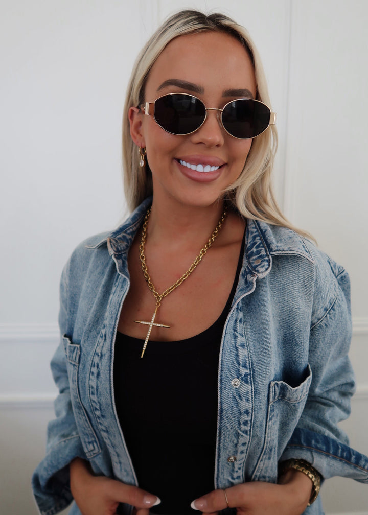 Woman wearing sunglasses, denim jacket, and black top against a white background
