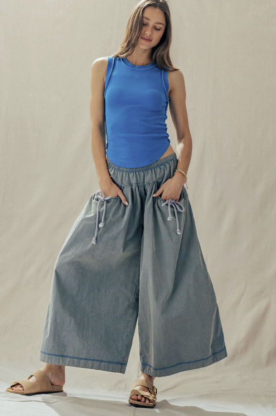 Woman wearing a blue sleeveless top and wide-leg gray pants against a plain background