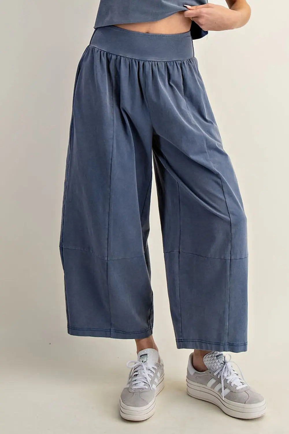 Person wearing blue wide-leg pants and gray sneakers on a plain background