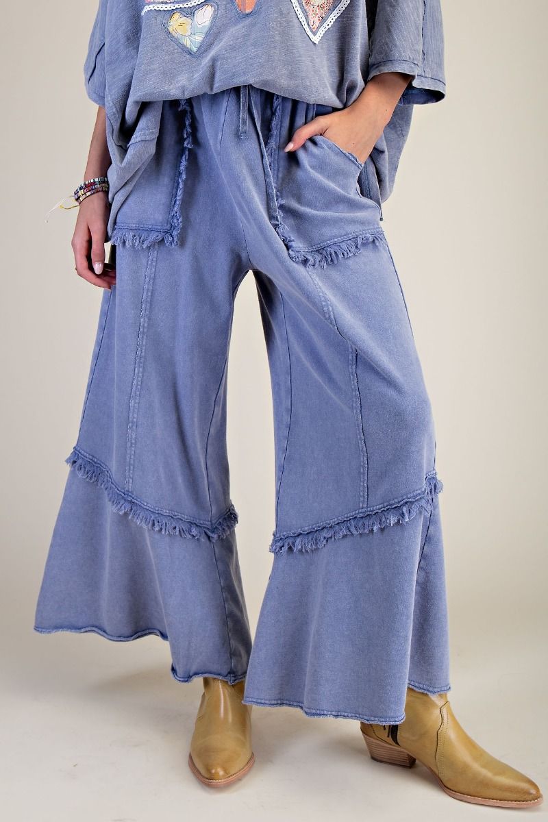 Person wearing blue denim flared pants with ruffled bottom hem on a plain background