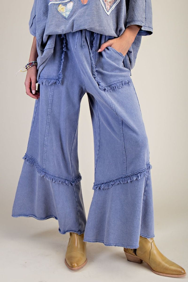 Person wearing blue denim flared pants with ruffled bottom hem on a plain background