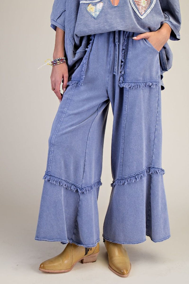 Person wearing a denim outfit with ruffled pants and embroidered top on a plain background