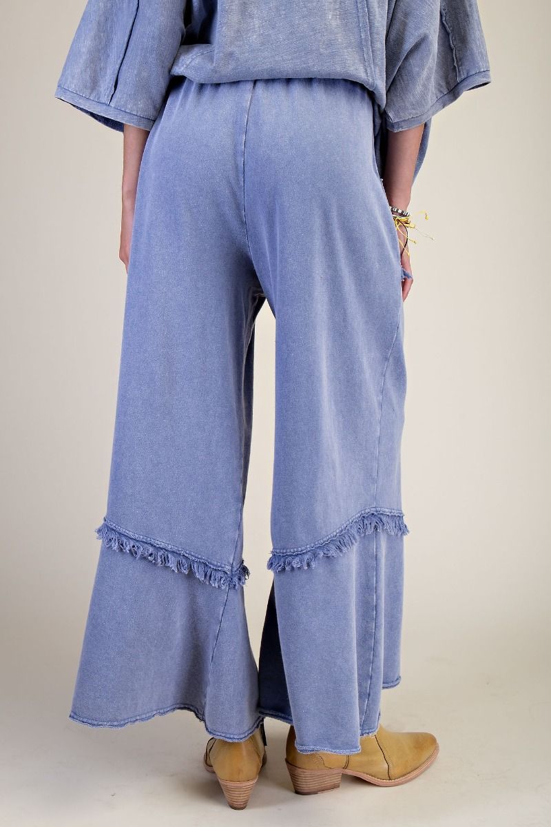 Person wearing light blue denim pants with ruffled bottom hem on a plain background