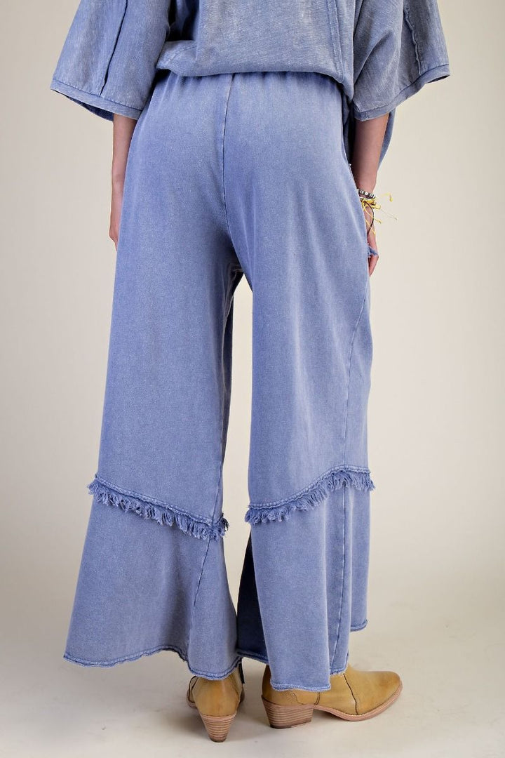 Person wearing light blue denim pants with ruffled bottom hem on a plain background