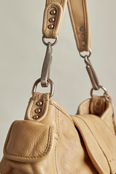 Close-up of a tan leather shoulder bag with a matching strap and silver-tone hardware, including a visible Bogg Bag logo on the metal clip.