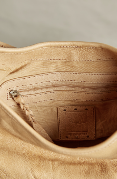 Close-up of the interior of a tan leather bag, showing a zippered pocket, braided zipper pull, and a square leather brand patch on the lining.