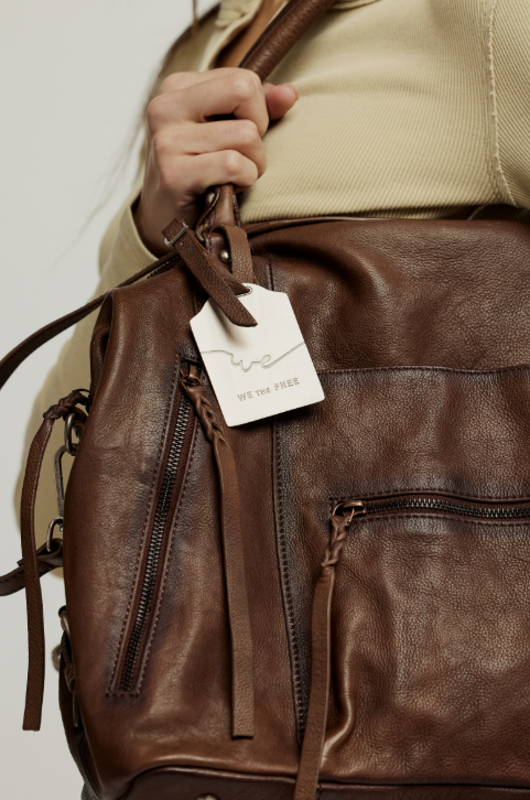 Brown leather backpack with a visible brand tag on a neutral background