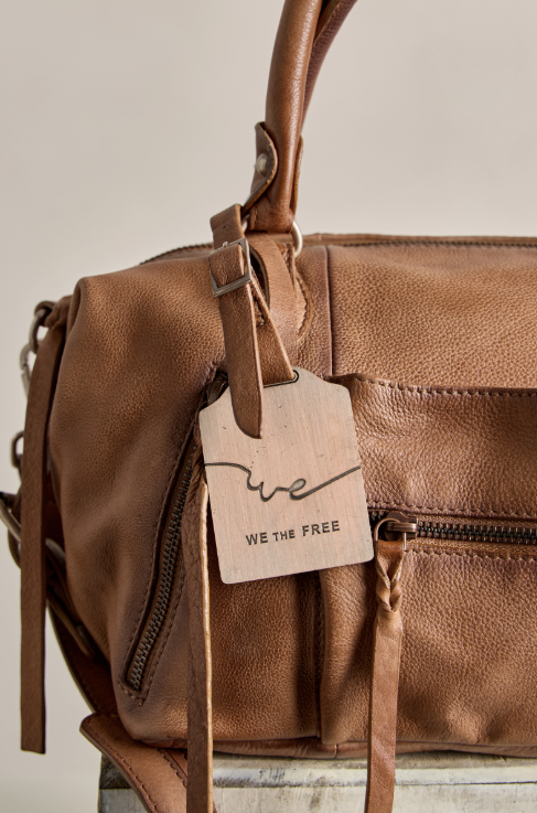 A close-up of a brown pebbled leather handbag with a hanging wooden tag that reads &