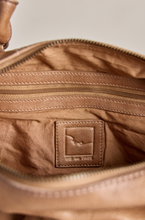 Close-up of the interior of a tan leather bag, showing a zippered pocket, stitched lining, and a square leather brand patch that reads &