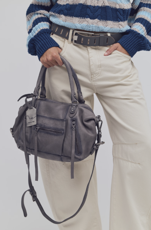 Woman holding grey purse wearing beige pants and blue striped top on white background