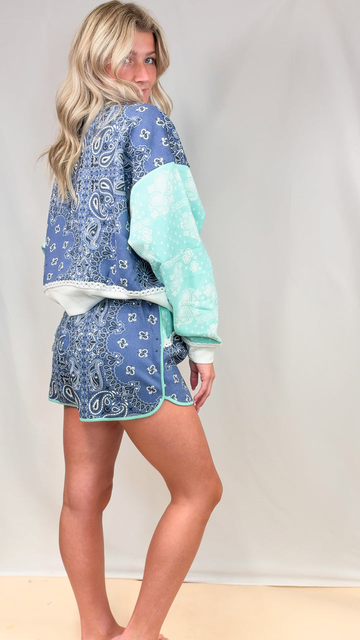 Woman wearing blue bandana print sweatshirt and sweatshorts set on plain background