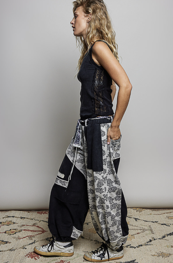 Woman wearing black tank top and black and white patch pants on plain background