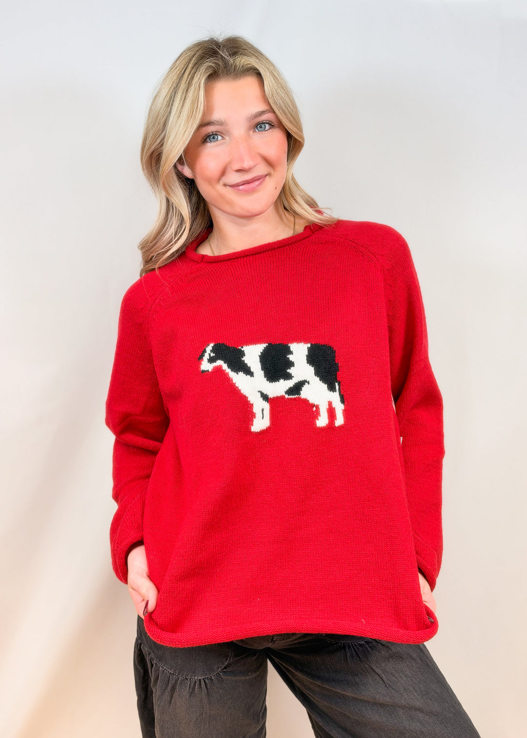 Woman wearing red sweater with cow design and black pants on plain background