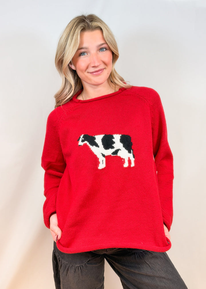 Woman wearing red sweater with cow design and black pants on plain background