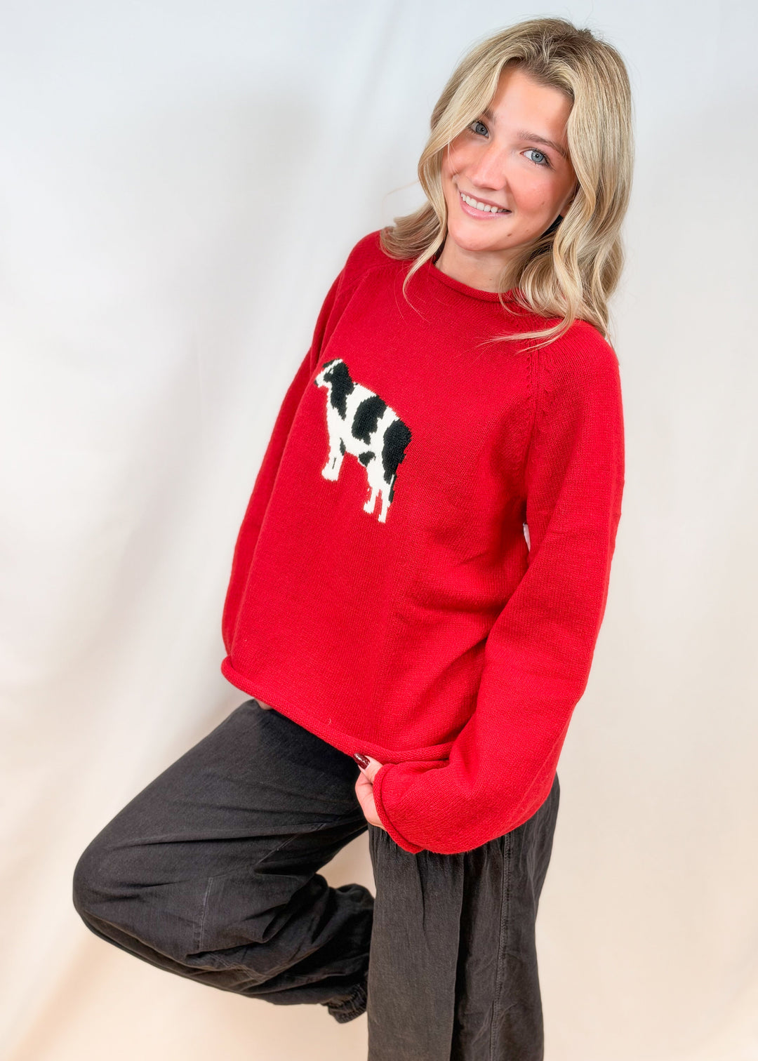 Woman wearing red sweater with cow design on front with black pants on plain background
