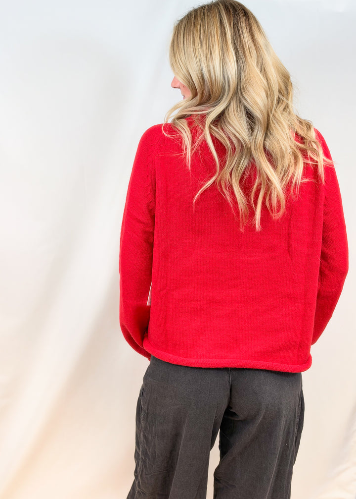 Woman shown from back view wearing red sweater and black pants on plain background
