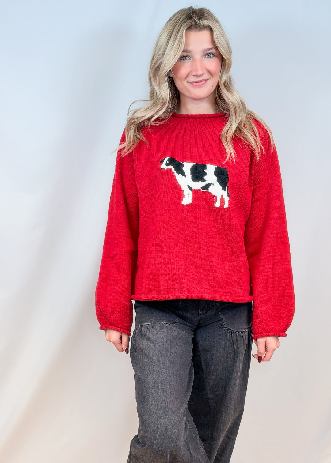 Woman wearing red sweater with cow design on front and black pants on plain background