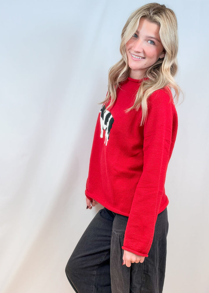 Woman shown from side view wearing red sweater and black pants on plain background