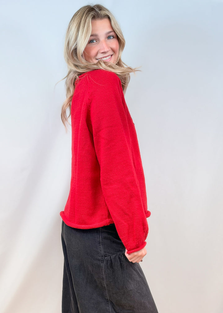 Woman shown from side view wearing red sweater and black pants on plain background