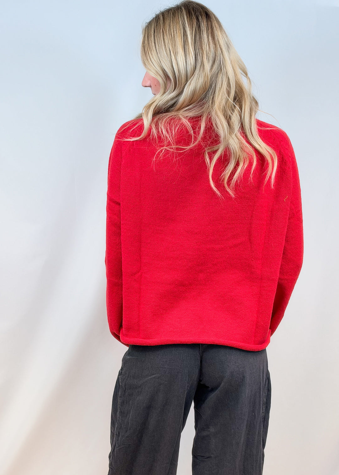 Woman shown from back wearing red sweater and black pants on plain background