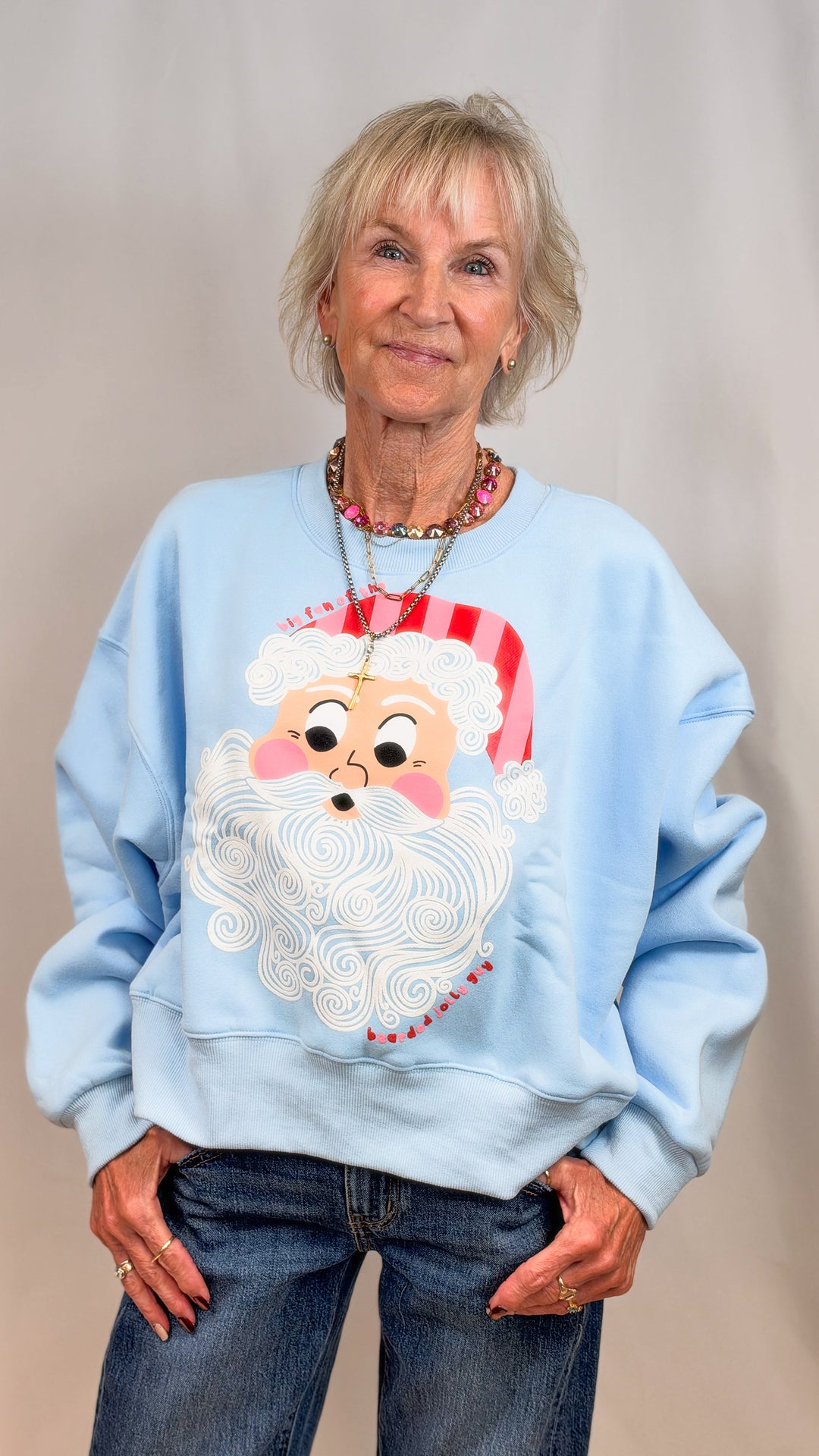 Woman wearing light blue sweatshirt with vintage santa face on plain background