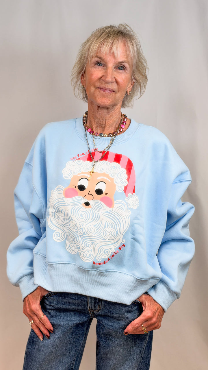 Woman wearing light blue sweatshirt with vintage santa face on plain background