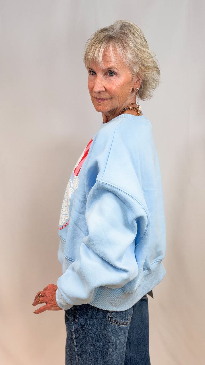 Woman shown from side view wearing light blue sweatshirt and jeans on plain background