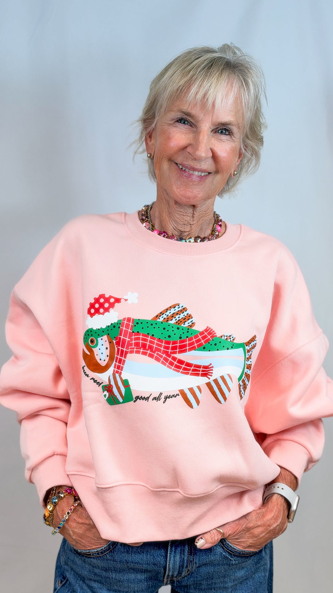 Woman wearing pink sweatshirt with fish graphic wearing santa hat on plain background