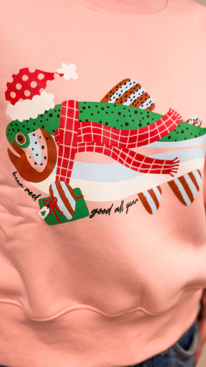Close up of woman wearing salmon color sweatshirt with fish graphic wearing santa hat and &