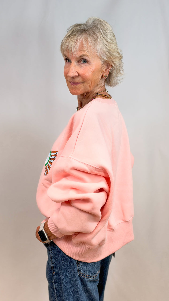 Woman shown from side view wearing salmon sweatshirt and jeans on plain background