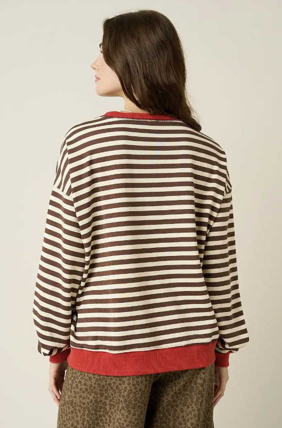 A woman shown from the back wearing a brown and cream horizontal striped long-sleeve sweatshirt with red ribbed trim at the collar, cuffs, and hem, paired with leopard-print pants against a plain light beige studio background.