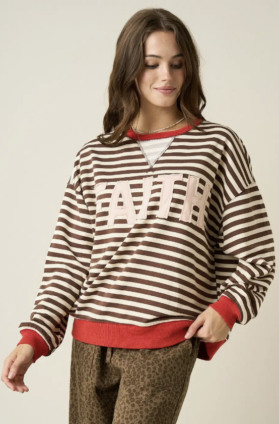 A woman wearing a brown and cream striped sweatshirt with red ribbed trim and a large cream &