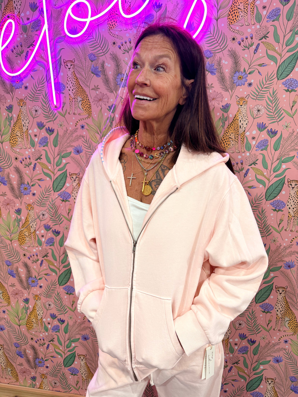 Woman wearing pink zip-up hoodie with blue stitching on hood on pink floral background