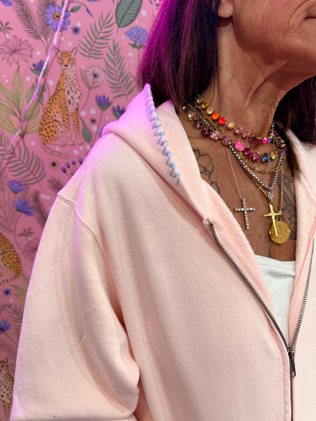 Close up of blue stitching on pink hoodie on pink floral background