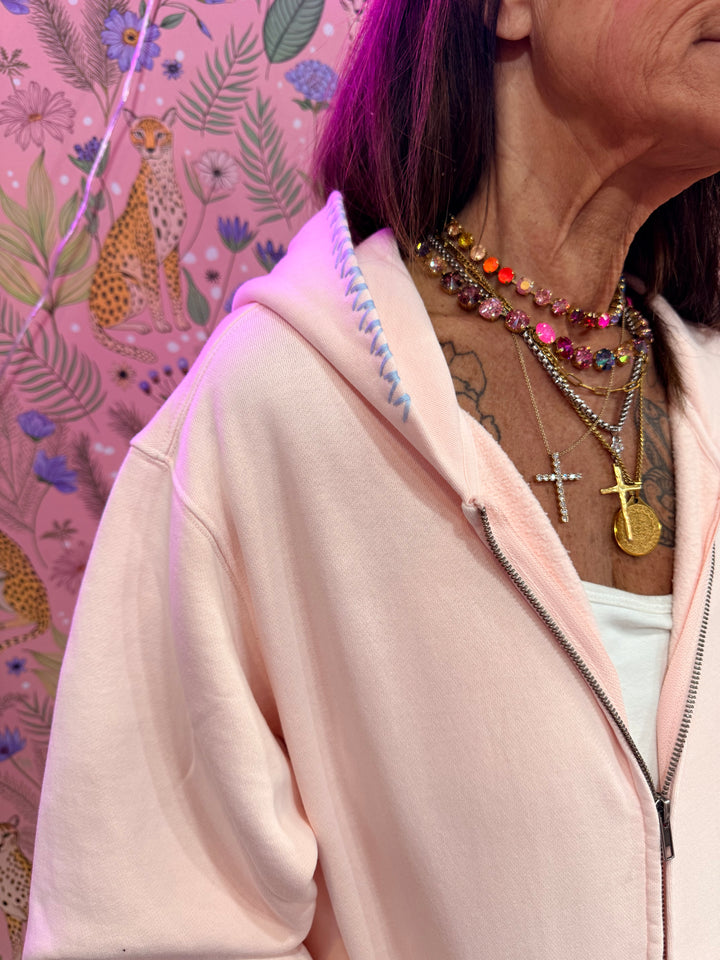 Close up of blue stitching on pink hoodie on pink floral background
