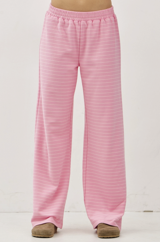Pink wide-leg lounge pants with thin white horizontal stripes, shown on a model from the waist down wearing brown slippers against a white studio background.