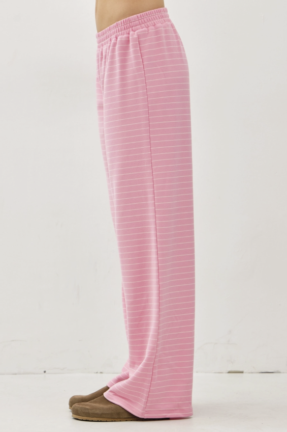 Pink wide-leg lounge pants with thin white horizontal stripes, shown on a model from the waist down wearing brown slip-on shoes against a plain white studio background.